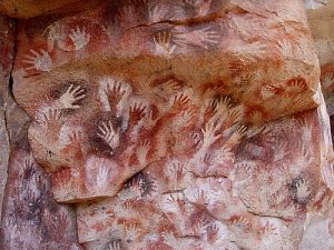 A photograph of prehistoric stencil paintings of human hands on a cave wall.