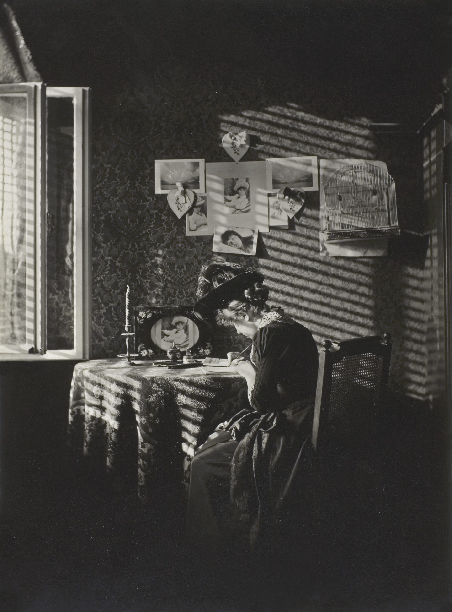 A black and white portrait of a woman sitting at a desk, with rays of sun from blinds at the window covering her.